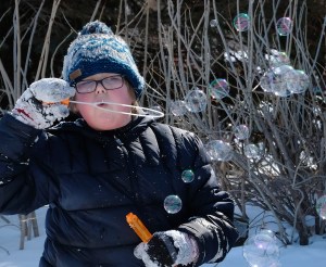 Boy in snow blows bubbles