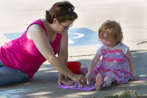 Woman and girl drawing on sidewalk.